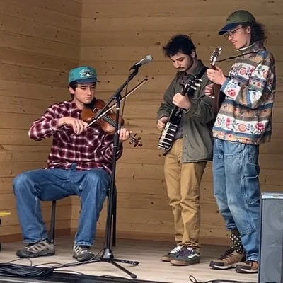 Three students play bluegrass music on a stage in the Art Cart