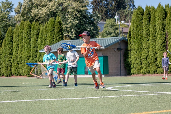 Children playing lacrosse on turf field.