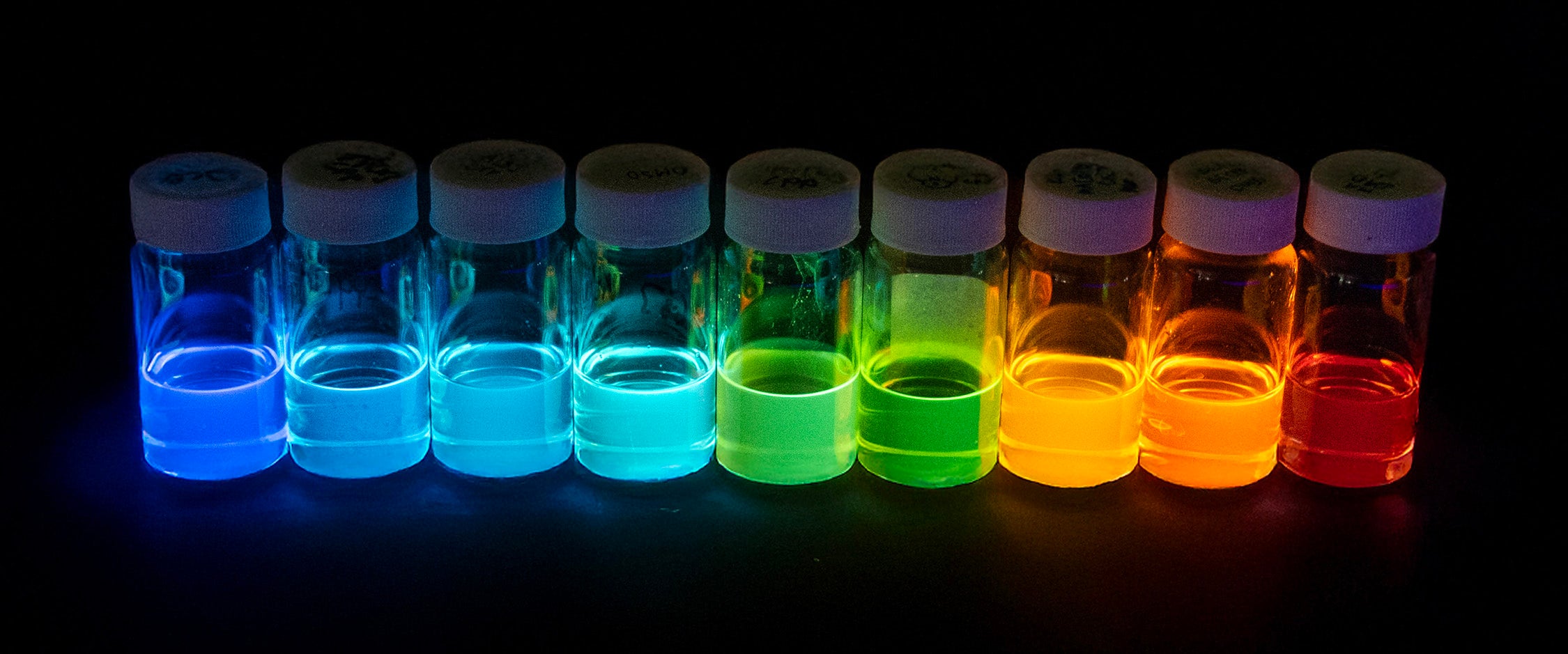 Sample containers full of fluorescent liquid arranged in order by color.