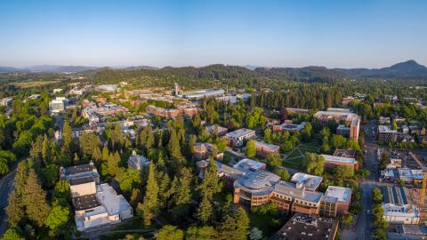 A panoramic, aerial view of the UO campus, with Spencer Butte in view in the distance.