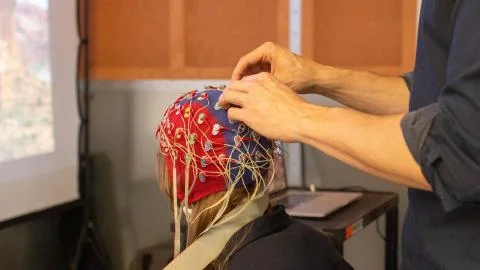 Research participant sits in a chair and has an electroencephalogram (EEG) cap placed on their head.  