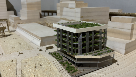 A diorama of a building with plants growing on it. The building and surrounding structures are made of wood.