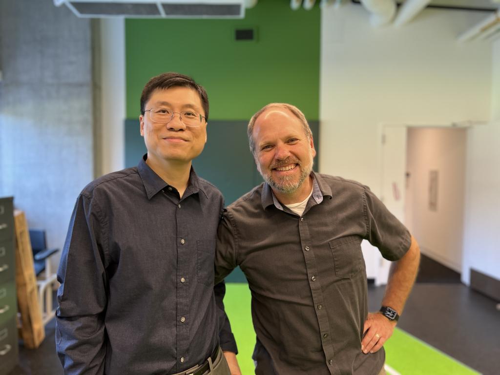 Two men smile side by side 