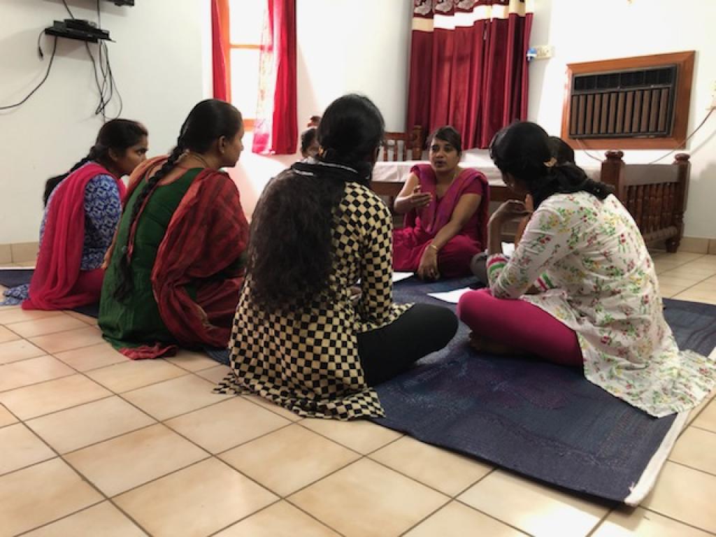 Women gather in a seated circle around a woman who is talking.