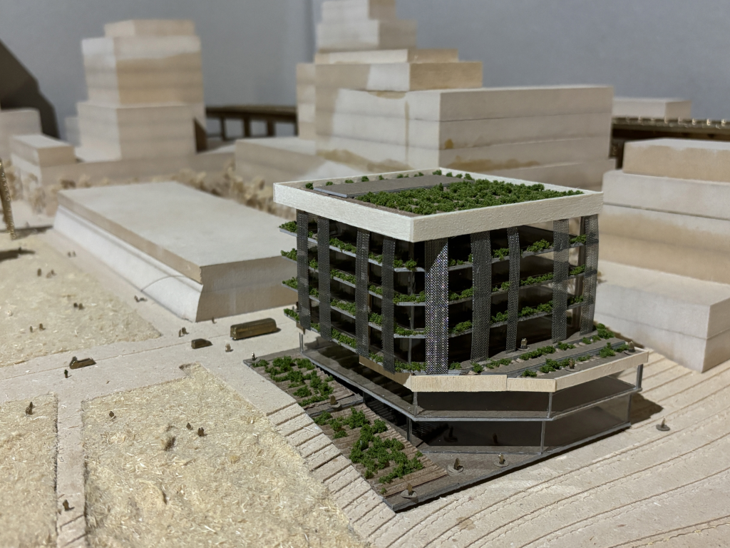 A diorama of a building with plants growing on it. The building and surrounding structures are made of wood.