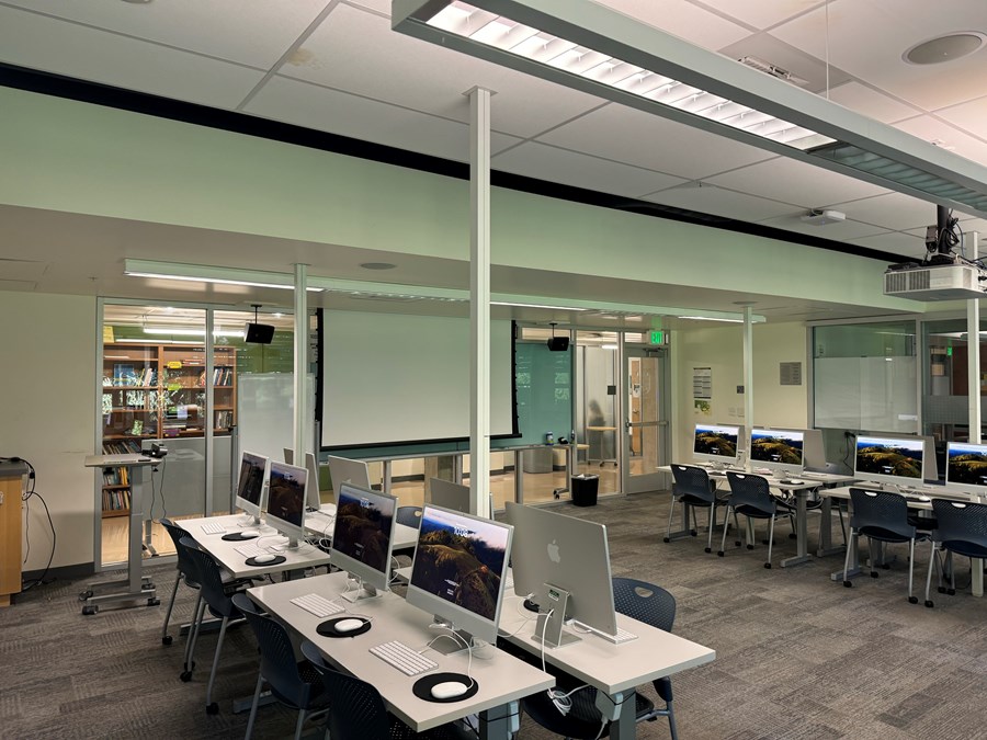 Image of Allen 303 with computers on desks, a projector screen open on the far wall, and the exit to the right