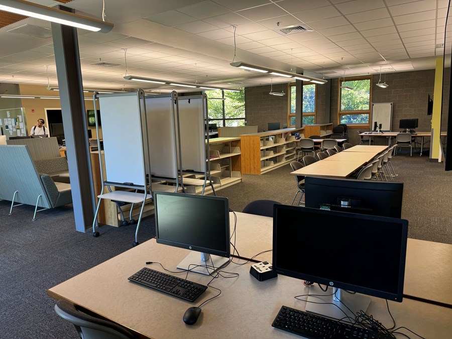 The HEDCO learning commons with three computers on desks in the forefront, rolling whiteboards, and other desks.
