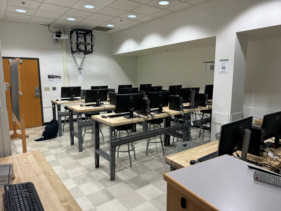 Lawrence 100: computers on desks with the exit on the back wall and the projector on the ceiling