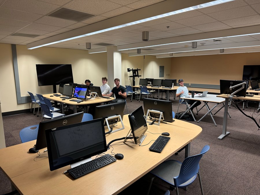 Edmiston computers on desks with students at desks giving the camera a thumbs up
