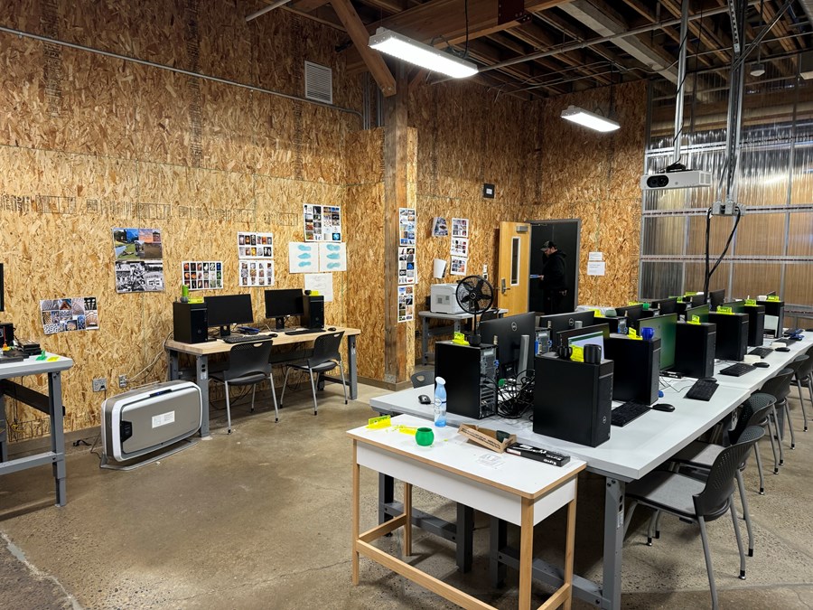 Image of Olive Lab with door on the back left and desks with computers and plastic chairs