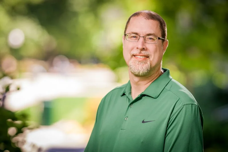 Man with a short beard wearing glasses and a green polo shirt