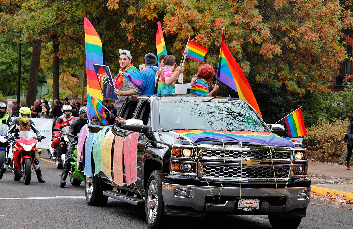 A group of students ride in a parade float supporting the LGBTQIA community.