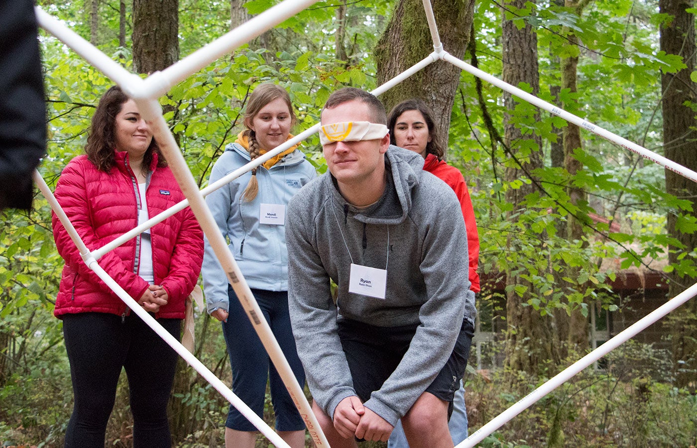 A blinded folded student navigates through a geometric shape with guidance from the students nearby.